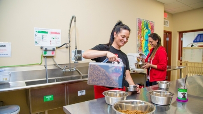 Two women in a kitchen measure out dog food