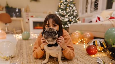 A woman lays with her pug on the floor, enjoying the cozy vibe of Christmas decorations as they welcome the New Year.