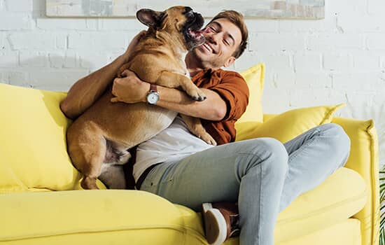 A man on a couch hugging a small dog