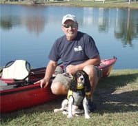Man kneeling next to boat and dog